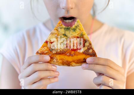 Une adolescente mange de la pizza. fille tient une pizza dans ses mains et mange dans un café de trottoir. Concept de Street food et fast-food. Régime alimentaire malsain comme cause de Banque D'Images