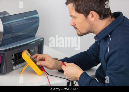 homme testant une imprimante cassée avec un multimètre Banque D'Images