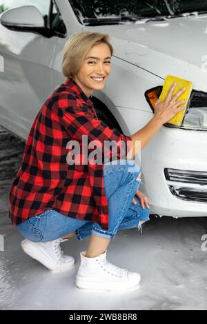 Jeune femme blonde nettoyant les phares de voiture Banque D'Images