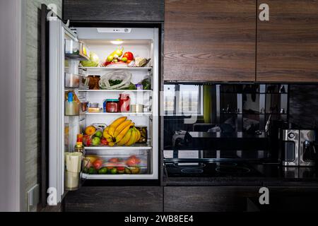 Ouvrir grand réfrigérateur avec des produits dans la cuisine noire. Banque D'Images