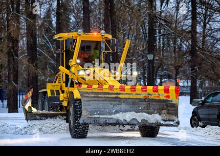 Niveleuse jaune Veekmas FG 2327 S enlevant la neige de la place de stationnement avec lame réglable après la chute de neige hivernale. Salo, Finlande. 27 décembre 2023. Banque D'Images