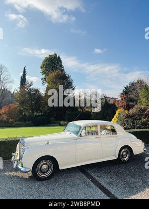 Milan, Italie - 12 novembre 2023 : White Rolls-Royce Silver Cloud se dresse sur un chemin de gravier près de buissons verts dans le parc Banque D'Images