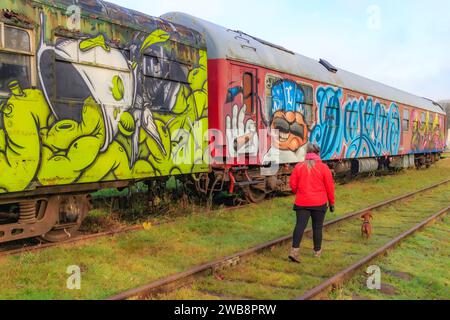 AS, Limbourg, Belgique. 17 décembre 2023. Vue arrière d'une femme marchant avec son chien entre les voies ferrées désaffectées de la vieille gare, voitures de tourisme peintes W Banque D'Images