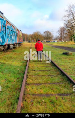 AS, Limbourg, Belgique. 17 décembre 2023. Voies ferrées désaffectées de la vieille gare avec femme marchant avec son chien, retour à la caméra, voitures de tourisme peintes W Banque D'Images