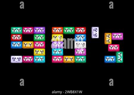 Texte carré '90' sur fond noir isolé, composé de cassettes audio anciennes, différentes et colorées. L'année de la nostalgie pour le hom analogique Banque D'Images