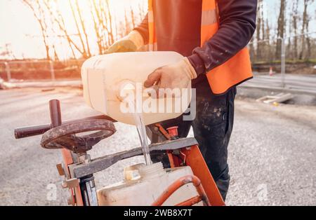 Gros plan et mise au point sélective du constructeur remplissant l'eau dans le réservoir d'eau de la tronçonneuse à essence pour couper la surface asphaltée des routes Banque D'Images