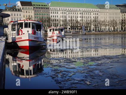 Hambourg, Allemagne. 09 janvier 2024. Les bateaux Alster sont entourés d'une fine couche de glace sous un soleil éclatant sur la Jungfernstieg sur l'Inner Alster. L'Hôtel Vier Jahreszeiten peut être vu en arrière-plan. Crédit : Christian Charisius/dpa/Alamy Live News Banque D'Images