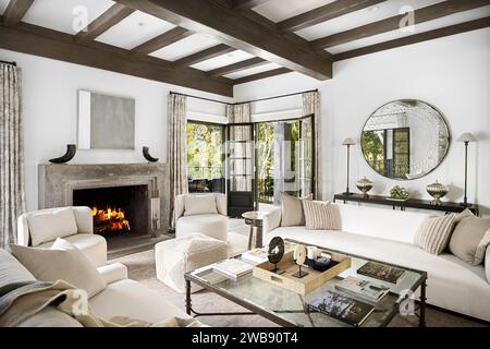 Un design intérieur d'un salon avec des canapés en cuir blanc avec une table basse en verre rectangulaire devant une cheminée en pierre blanche Banque D'Images