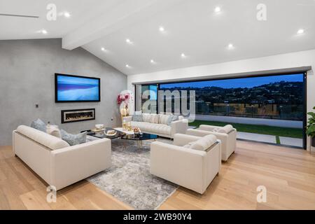 Ce salon contemporain présente deux canapés élégants et deux tables d'extrémité à côté d'une grande fenêtre, offrant une abondance de lumière naturelle Banque D'Images