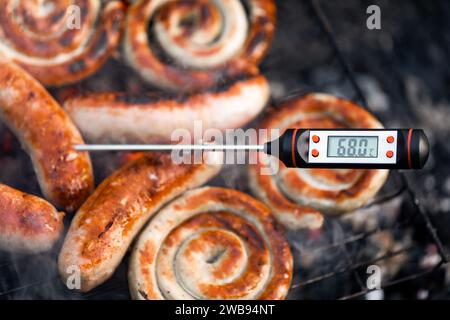 Сlose-plan d'un thermomètre à viande numérique affichant une température de cuisson sécuritaire des saucisses cuites sur un gril à fumée Banque D'Images