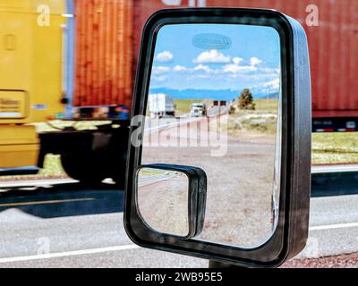 Un rétroviseur latéral à l'avant d'une voiture est visible, avec plusieurs camions visibles en arrière-plan Banque D'Images