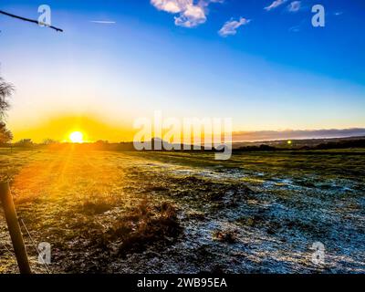 Un magnifique coucher de soleil aux teintes roses et oranges illuminant le ciel au-dessus d'une petite ferme située sur la côte Banque D'Images