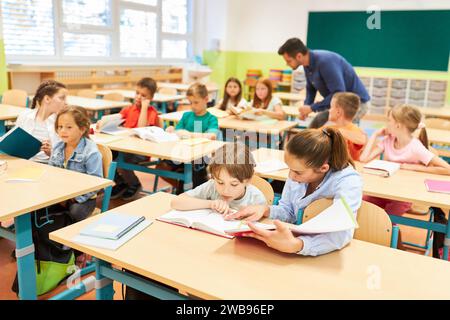 Enseignante de sexe féminin lisant le livre à une écolière du primaire alors qu'elle était assise sur un banc dans la salle de classe Banque D'Images
