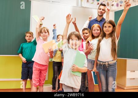 Groupe d'écoliers heureux levant la main en classe Banque D'Images