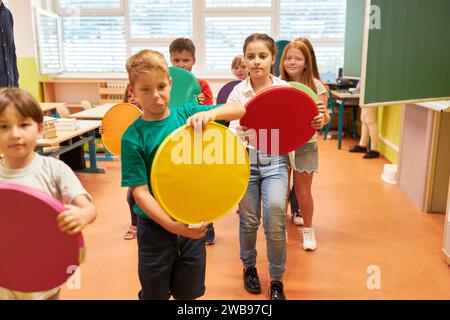 Groupe d'écoliers élémentaires marchant tout en tenant des coussins de siège colorés dans la salle de classe Banque D'Images