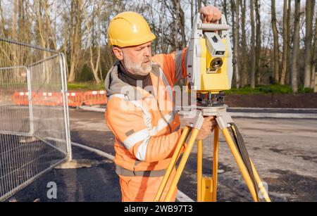 Ingénieur de chantier réglant son instrument pendant les travaux routiers. Constructeur installant le tachymètre de station de positionnement total sur le chantier de construction pour la nouvelle route setti Banque D'Images