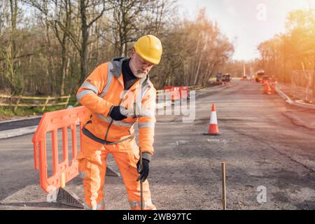 Le constructeur défonce la route en posant des goupilles en acier avec un marteau en morceaux pendant les travaux routiers. Constructeur martelant des barres d'acier dans l'asphalte pendant le roadwor Banque D'Images