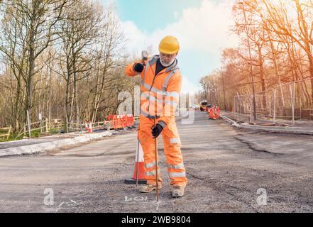 Le constructeur défonce la route en posant des goupilles en acier avec un marteau en morceaux pendant les travaux routiers. Constructeur martelant des barres d'acier dans l'asphalte pendant le roadwor Banque D'Images