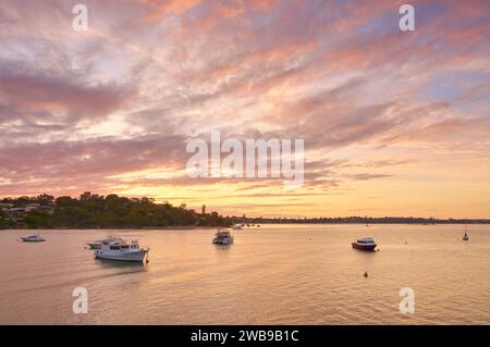 Une vue depuis Blackwall Reach à Bicton sur la rivière Swan au coucher du soleil avec des nuages colorés et le ciel et des bateaux sur l'eau, Perth, Australie occidentale. Banque D'Images