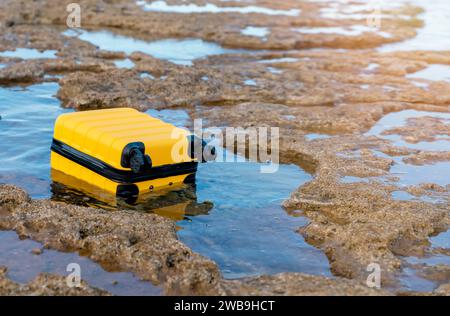 Valise jaune flottant dans la mer par beau temps. Assurance voyage et concept de bagages perdus. Banque D'Images