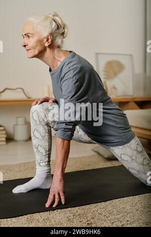 Vue latérale d'une femme active mature regardant vers l'avant tout en se tenant debout sur le tapis avec une jambe pliée dans le genou et l'autre étirée vers l'arrière Banque D'Images