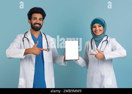 Application médicale Couple de médecins arabes pointant vers la tablette numérique avec écran vide Banque D'Images