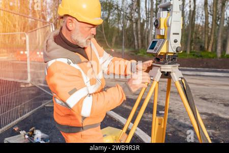 Ingénieur de chantier réglant son instrument pendant les travaux routiers. Constructeur installant le tachymètre de station de positionnement total sur le chantier de construction pour la nouvelle route setti Banque D'Images