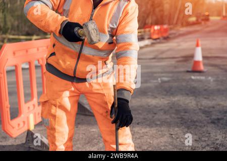 Le constructeur défonce la route en posant des goupilles en acier avec un marteau en morceaux pendant les travaux routiers. Constructeur martelant des barres d'acier dans l'asphalte pendant le roadwor Banque D'Images