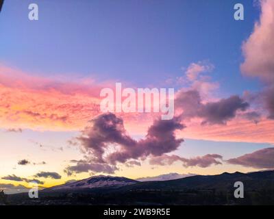 Une scène de nature à couper le souffle avec un ciel de coucher de soleil avec des nuages tourbillonnants au-dessus d'une gamme de majestueuses montagnes enneigées Banque D'Images