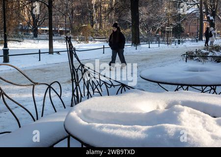 Cracovie, Pologne, 9 janvier 2024. Une jeune femme vêtue de couvertures hivernales passe devant un caffee couvert de neige dans le parc historique Planty dans le centre-ville alors que les températures chutent bien en dessous de zéro et que la neige recouvre la majeure partie de la ville. Crédit : Dominika Zarzycka/Alamy Live News. Banque D'Images