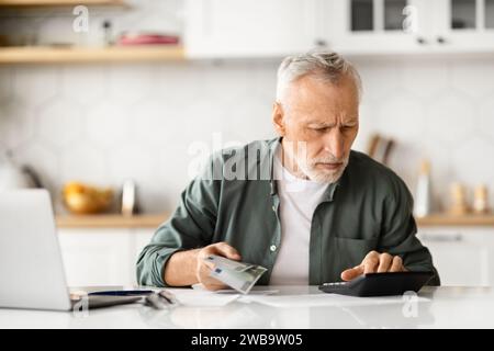 Homme senior concentré avec de l'argent en main calculant les finances à la maison Banque D'Images
