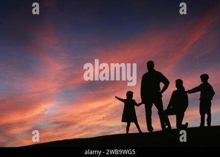 Silhouette d'une famille de quatre personnes debout sur une colline regardant de beaux nuages de coucher de soleil Banque D'Images