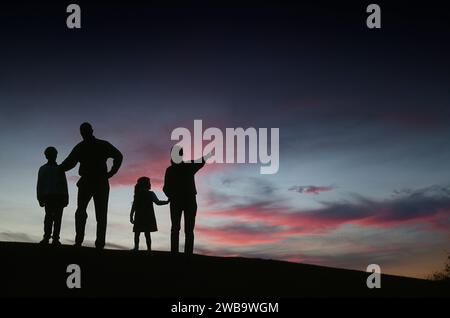 Silhouette d'une famille de quatre personnes debout sur une colline regardant de beaux nuages de coucher de soleil Banque D'Images