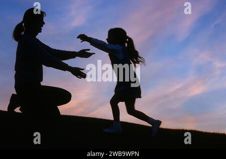 Une petite fille se profilait sur une colline et le coucher du soleil se précipitant vers ses mères attendant les bras Banque D'Images