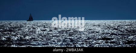 Une photographie panoramique d'un seul voilier naviguant aux Bahamas un soir éclairé par la lune Banque D'Images