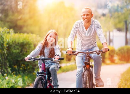 Portraits souriant père avec fille pendant l'été randonnée à vélo en plein air. Ils apprécient la convivialité dans le parc de la ville d'été. Bonne parentalité et chi Banque D'Images