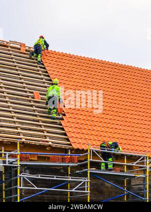 Trois couvreurs en vêtements de travail de protection installant de nouvelles tuiles d'argile, nouvelle couche de tuiles d'argile couvrant, installation de tuiles d'argile Banque D'Images