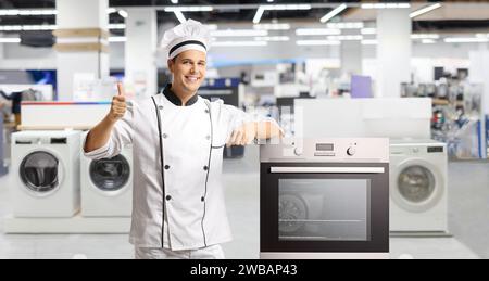 Chef masculin faisant des gestes de pouces vers le haut à côté d'un poêle dans un magasin Banque D'Images