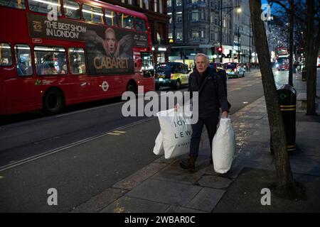 Un homme portant des sacs John Lewis brave le froid hivernal pendant les averses glaciales et de pluie sur Oxford Street, la rue la plus fréquentée de Londres. Banque D'Images