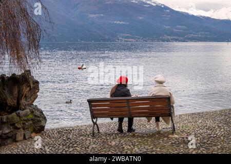 Jeunes amis assis sur un banc en bois devant le lac de Côme, Varenna, région des lacs, Lombardie, Italie Banque D'Images