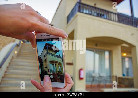 Femme prenant une photo d'une maison avec son smartphone. Vous pouvez voir la maison sur l'écran et ses mains avec le smartphone Banque D'Images