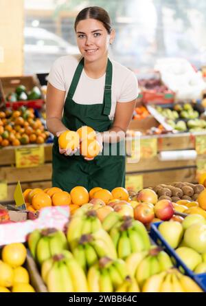 Jeune vendeuse souriante offrant des oranges mûres dans la boutique de fruits et légumes Banque D'Images