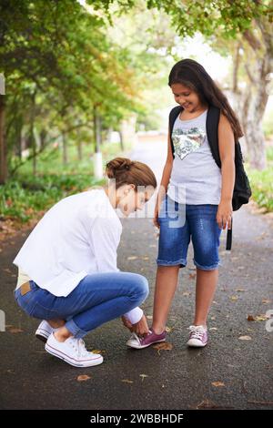 Femme, enseignant et attachant des chaussures d'étudiant dans le parc pour la rentrée des classes, l'apprentissage ou l'éducation dans la nature. Femme enseignant à une petite fille à nouer des lacets Banque D'Images