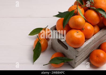 Délicieuses mandarines avec des feuilles dans la caisse sur la table en bois blanc, gros plan. Espace pour le texte Banque D'Images