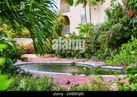 Piscine tropicale abandonnée avec verdure envahie et bâtiment négligé Banque D'Images