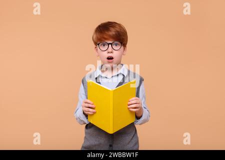 Écolier surpris avec le livre sur fond beige Banque D'Images