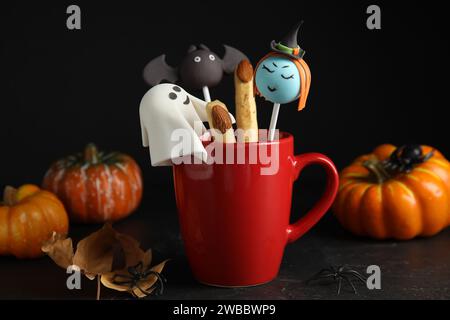 Différents types de gâteau dans une tasse décorée comme des monstres sur une table noire. Halloween Banque D'Images