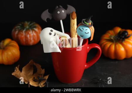 Différents types de gâteau dans une tasse décorée comme des monstres sur une table noire. Halloween Banque D'Images