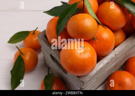 Délicieuses mandarines avec des feuilles dans la caisse sur la table en bois blanc, gros plan Banque D'Images