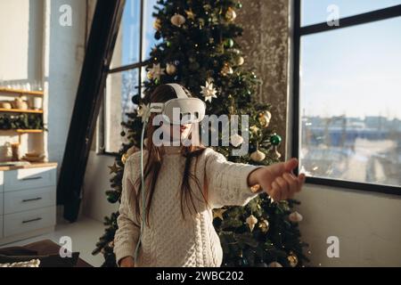 Le portrait représente une belle fille immergée dans la réalité virtuelle, posée contre un sapin de Noël. Banque D'Images
